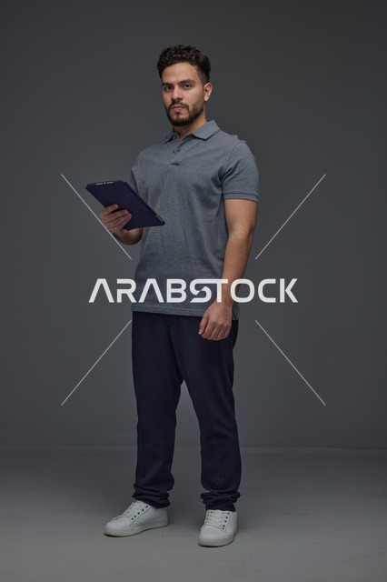 رجل سعودي يحمل جهازًا لوحيًا أمام خلفية استوديو داكنة