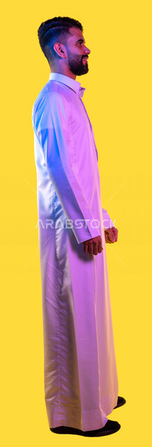 بورتريه من الجانب لشاب عربي خليجي سعودي يقف بإستقامة وثقة ، صورة بالطول الكامل ، كامل الجسم ، خلفية صفراء