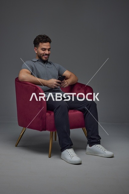 رجل سعودي يستخدم الهاتف الذكي جالساً على كرسي أحمر
