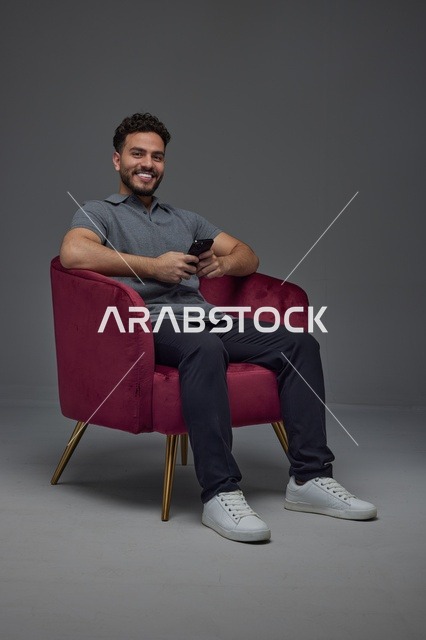 رجل سعودي يبتسم ويستخدم الهاتف الذكي في الاستوديو