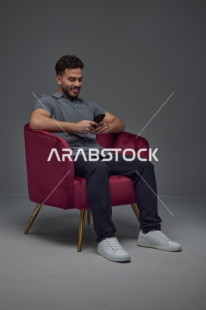 رجل سعودي يجلس على كرسي ويستخدم الهاتف الذكي