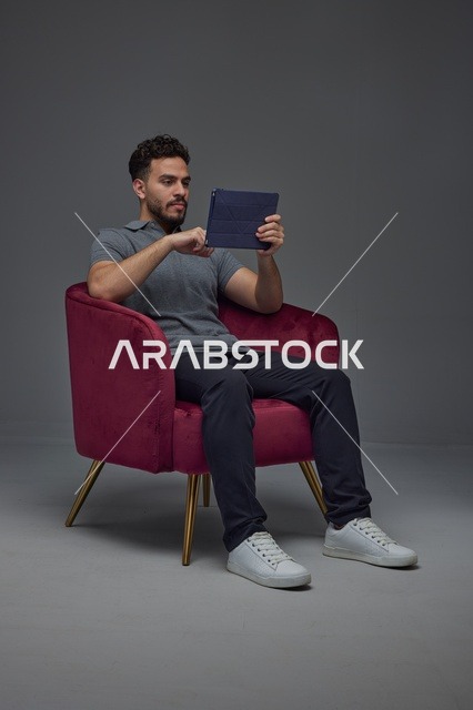 رجل سعودي يجلس على كرسي يستخدم جهازاً لوحياً