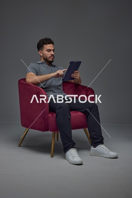 Saudi Man Using Tablet in Red Armchair