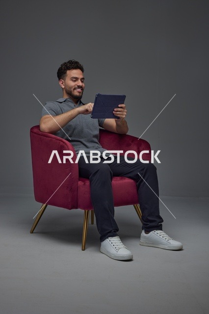 Saudi Man Using Digital Tablet on Red Armchair