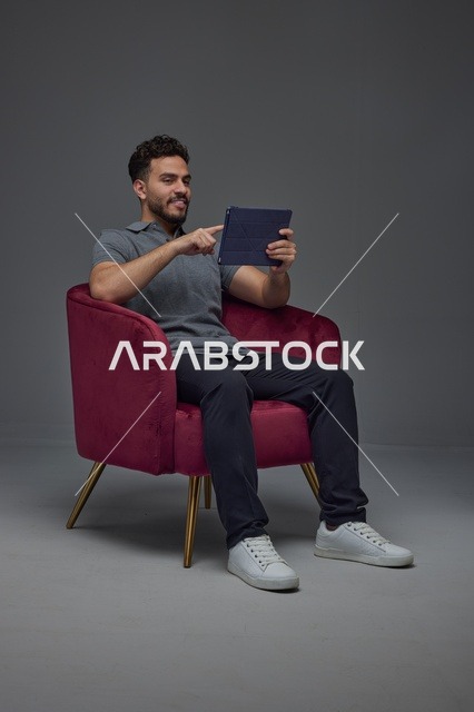 Saudi Man Using Digital Tablet in Grey Studio Armchair