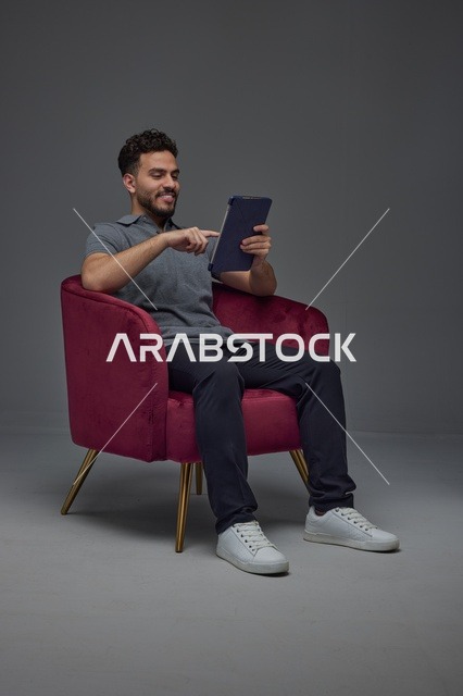 Saudi Man Using Digital Tablet in Red Armchair Studio