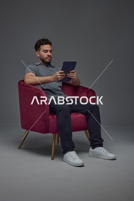Saudi Man Using Tablet in Red Armchair