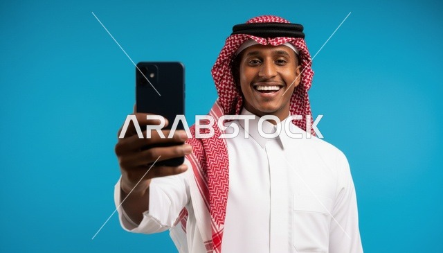 رجل سعودي مبتسم يلتقط صورة سيلفي أمام خلفية زرقاء
