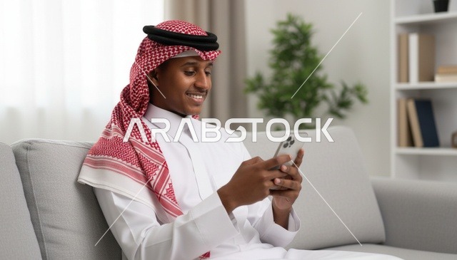 رجل سعودي بالثوب يستخدم الهاتف الذكي على الأريكة