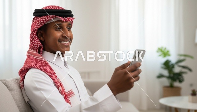 رجل سعودي مبتسم يستخدم الهاتف الذكي في غرفة معيشة