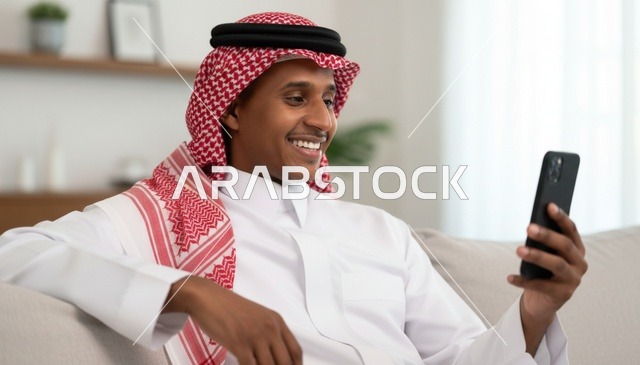 رجل سعودي يستخدم الهاتف الذكي بالثوب والشماغ داخل المنزل