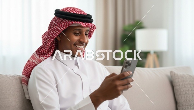 رجل سعودي بالثوب التقليدي يستخدم الهاتف الذكي في المنزل