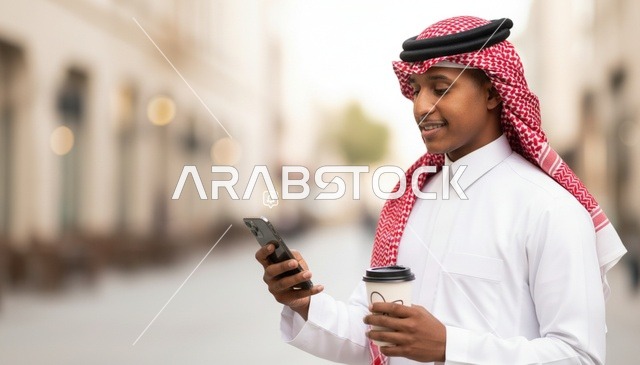 رجل سعودي يستخدم الهاتف الذكي ويمسك قهوة