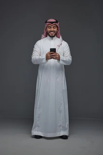 رجل سعودي بالثوب التقليدي يستخدم الهاتف الذكي بابتسامة