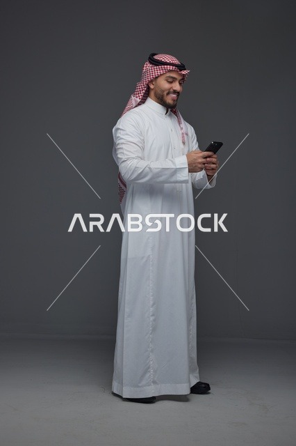 رجل سعودي يستخدم الهاتف الذكي بخلفية استوديو رمادية