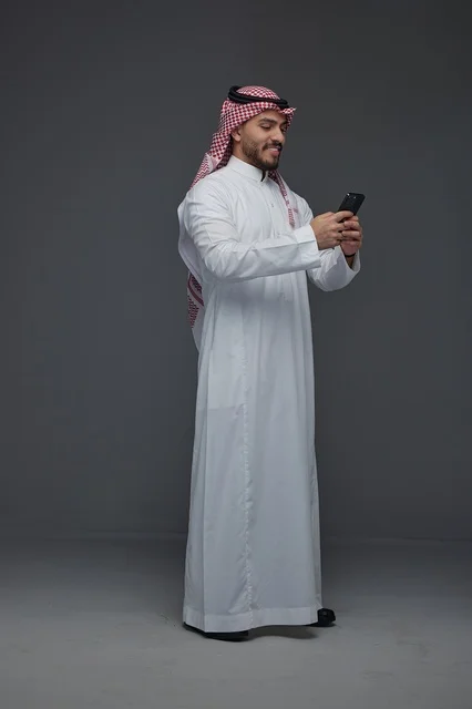 رجل سعودي بالثوب التقليدي يستخدم الهاتف الذكي