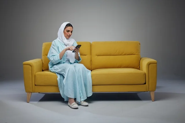 امرأة سعودية تجلس على الأريكة تستخدم الهاتف الذكي