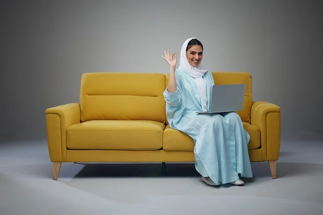 Saudi Woman Sitting on Sofa Using Laptop and interacting with the camera