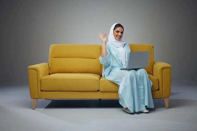 Saudi Woman Sitting on Sofa Using Laptop and interacting with the camera