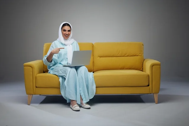 Saudi Woman Sitting on Sofa Using Laptop and interacting with the camera