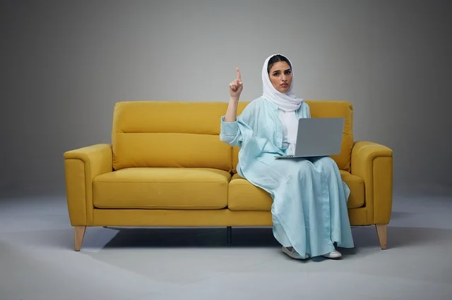 Saudi Woman with Laptop Sitting on Yellow Sofa