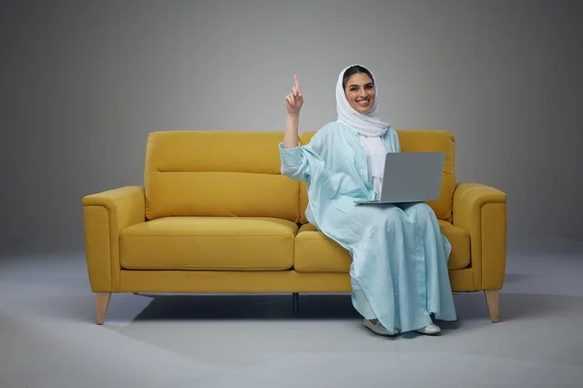امرأة سعودية مع حاسوب محمول على أريكة صفراء