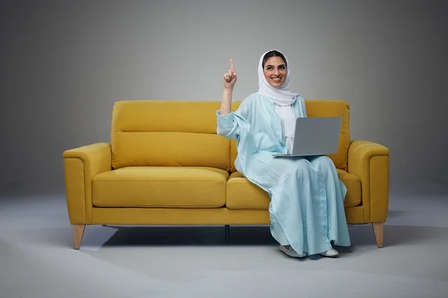 Saudi Woman Sitting on Sofa Using Laptop and interacting with the camera