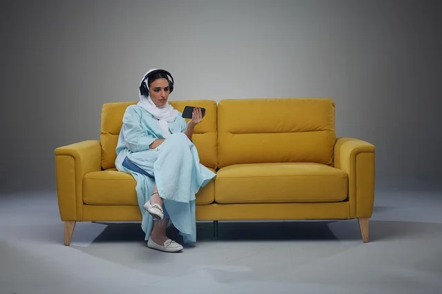 امرأة سعودية على أريكة صفراء مع سماعات وهاتف
