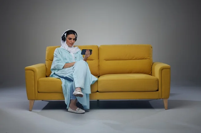امرأة سعودية تجلس على الأريكة وتستخدم الهاتف مع سماعات الرأس