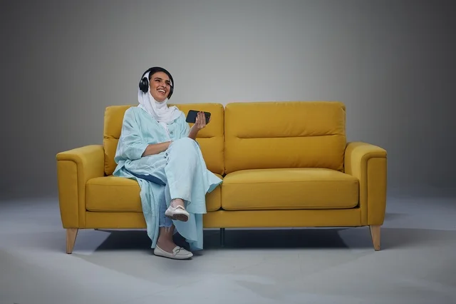 امرأة سعودية تستخدم الهاتف وسماعات الرأس على الأريكة