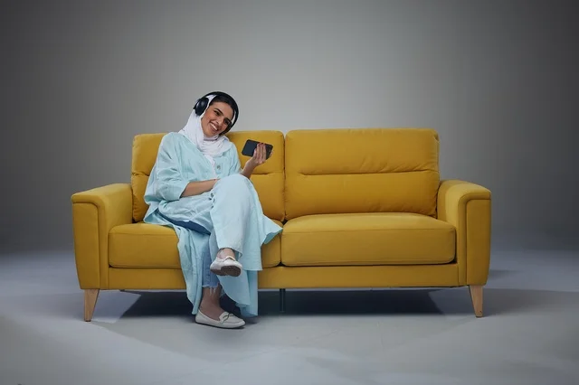 Saudi Woman on Yellow Sofa with Headphones and Phone