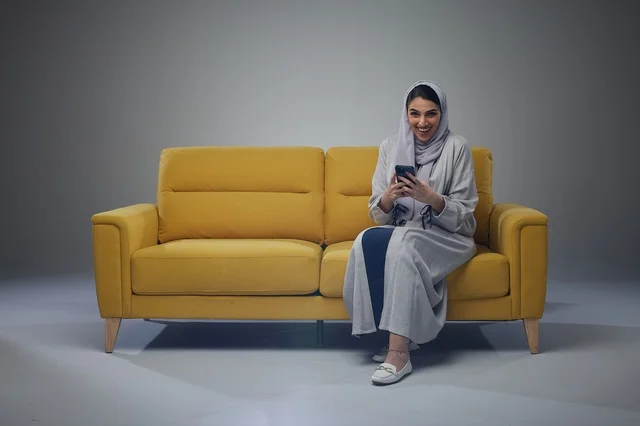 امرأة سعودية تستخدم الجوال على أريكة صفراء