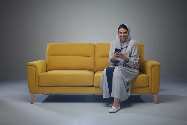 امرأة سعودية تستخدم هاتف ذكي جالسة على أريكة صفراء