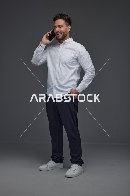 رجل سعودي يتحدث عبر الهاتف الذكي في استوديو رمادي