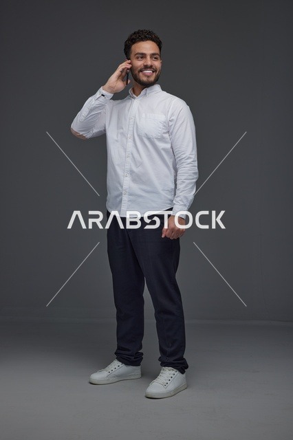 رجل سعودي يتحدث عبر الهاتف الذكي في استوديو بخلفية رمادية