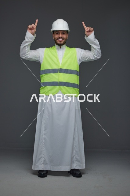 مهندس سعودي يرتدي سترة السلامة يشير للأعلى في استوديو