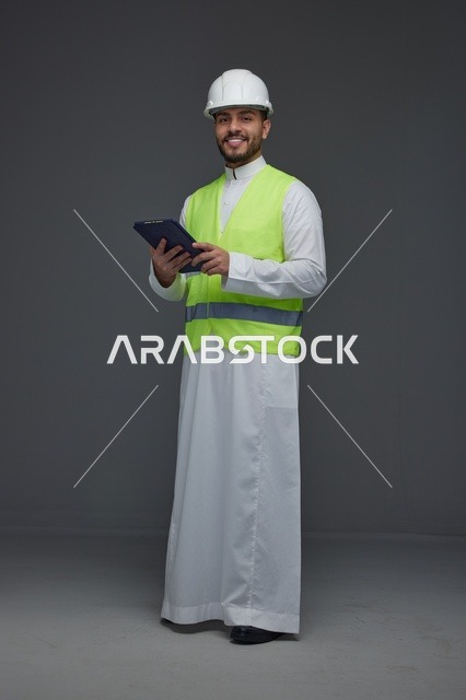 مهندس سعودي يرتدي سترة السلامة ويحمل جهازاً لوحياً