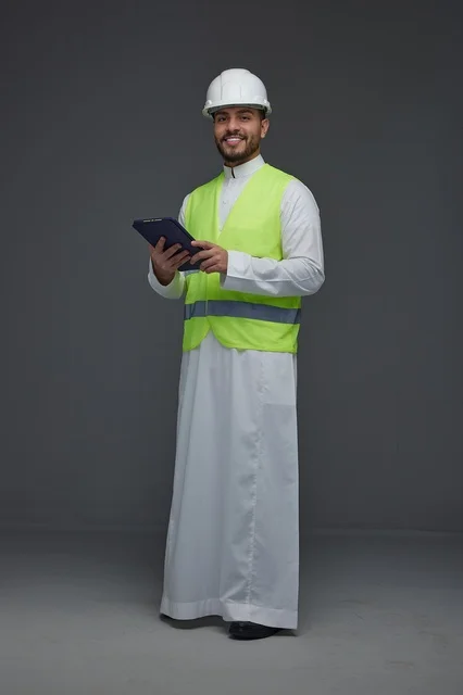 مهندس سعودي يرتدي سترة السلامة ويحمل جهازاً لوحياً