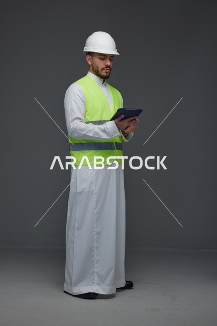 مهندس سعودي يرتدي سترة السلامة ويستخدم جهاز لوحي