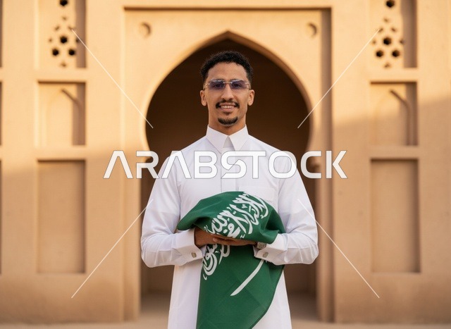 رجل سعودي يحمل العلم في موقع تراثي تقليدي