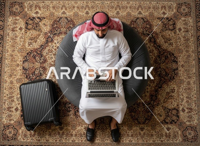 رجل سعودي يعمل على المحمول بجانب حقيبة السفر منظور علوي