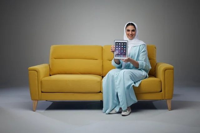 Saudi Woman on Yellow Sofa Holding Tablet Studio Shot