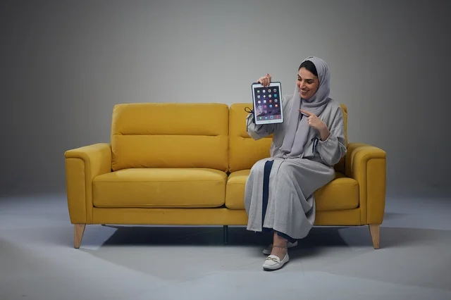Saudi Woman Pointing at Digital Tablet on Yellow Sofa