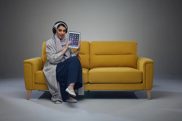 امرأة سعودية مع جهاز لوحي على أريكة صفراء
