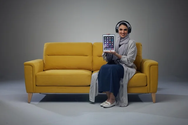 Saudi Woman on Yellow Sofa Holding Tablet with Headphones