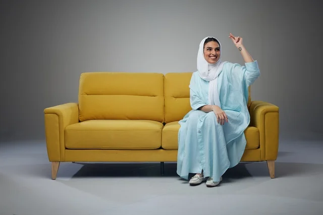 امرأة سعودية تجلس على أريكة صفراء وتشير