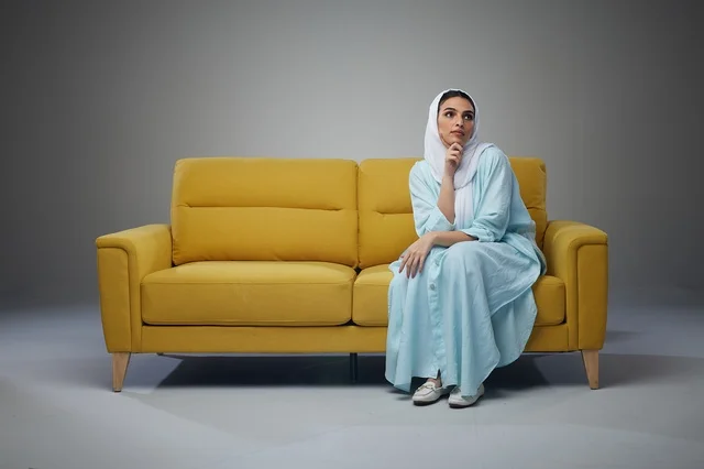 امرأة سعودية بعباءة تجلس على أريكة صفراء
