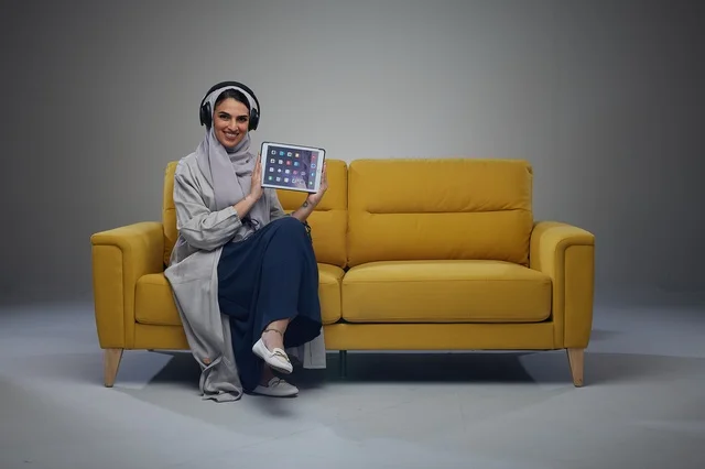 امرأة سعودية على أريكة صفراء تعرض شاشة جهاز لوحي