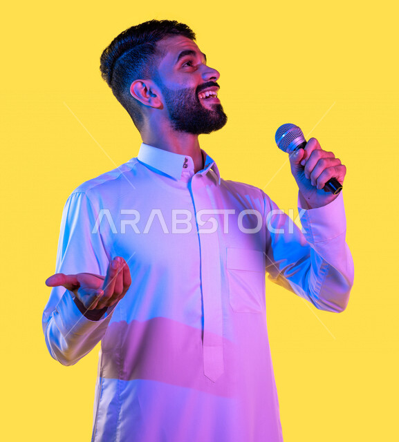 بورتريه لشاب عربي خليجي سعودي يمسك بيده المايكروفون و يغني بإيماءات تدل على السعادة و الانسجام بالغناء ، موهبة وفن ، رفاهية و ترفيه ، أغاني و طرب ، خلفية صفراء