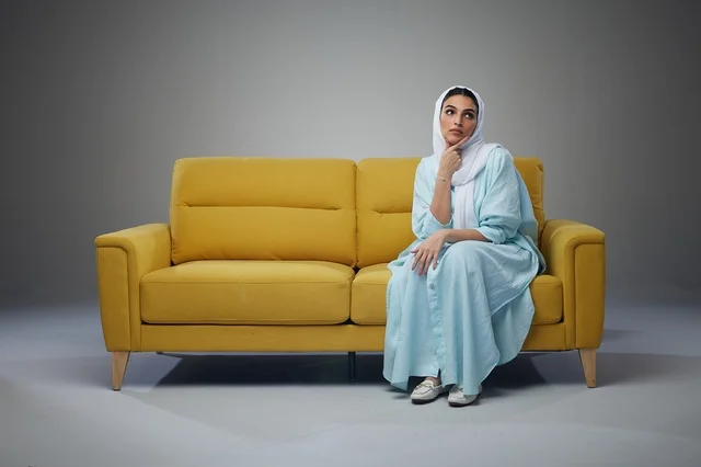 Saudi Woman Thinking on Yellow Sofa in Neutral Studio